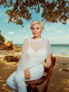 Woman in white sitting on a wooden chair on a beach.