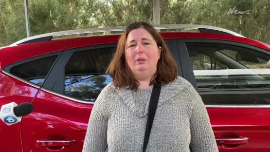Woman being interviewed by a news reporter, standing next to a red car.