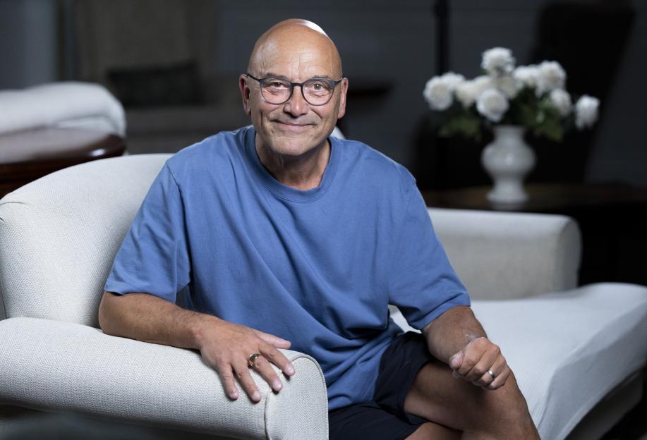 Gregg Wallace wearing glasses and a blue shirt, sitting on a light-colored couch.