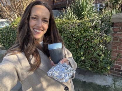 Woman holding a reusable coffee cup and food wrapped in foil.