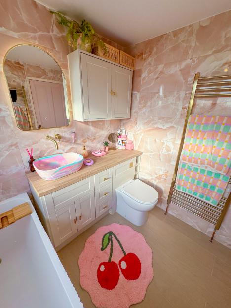 Pink bathroom with a pastel pink and white sink and cherry-patterned rug.