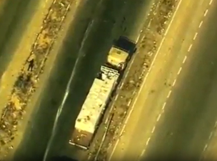 Aerial view of a truck on a highway with a person standing on the shoulder.