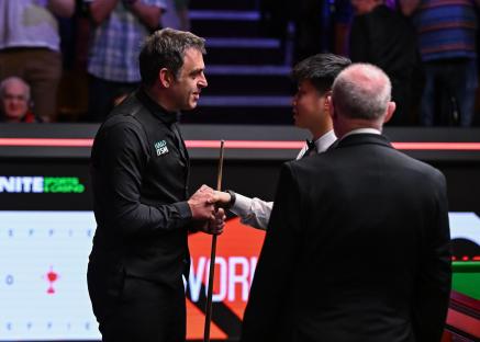 Ronnie O'Sullivan and Zhao Xintong shaking hands after a snooker match.