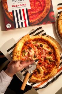 A hand holds a slice of pizza with olives and ham.