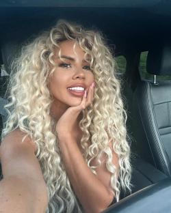 Woman with long blonde curly hair in a car.