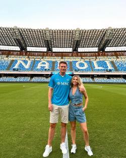 Couple standing on a soccer field in front of a stadium.