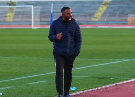 Man in dark blue jacket coaching on soccer field.