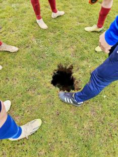 Soccer players surrounding a sinkhole on a field.