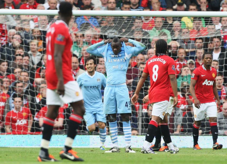 Mario Balotelli celebrates scoring a goal, revealing a shirt that says "Why Always Me?"