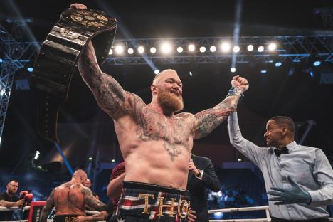 Eddie Hall holding up a championship belt after a boxing match.