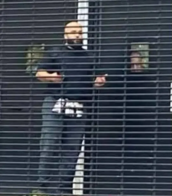 A man in a black shirt behind horizontal bars, possibly holding a phone.