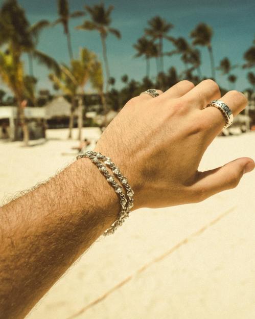 Hand wearing bracelets and rings on a beach.