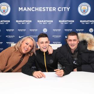 Phil Foden signing a document with his parents.