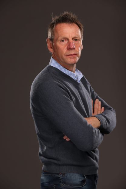 Man in a blue sweater and plaid shirt with his arms crossed.