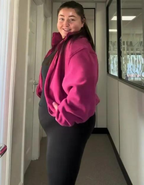 A woman in a magenta jacket and black leggings shows off her weight loss.