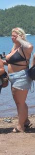 Woman in a black bikini top and denim shorts on a beach.