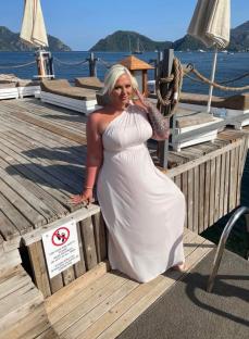 Woman in a white maxi dress on a dock overlooking the sea.