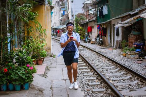 Person walking down a train track in Hanoi's Old Quarter, using a smartphone.