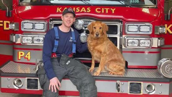 Firefighter with dog in front of firetruck.