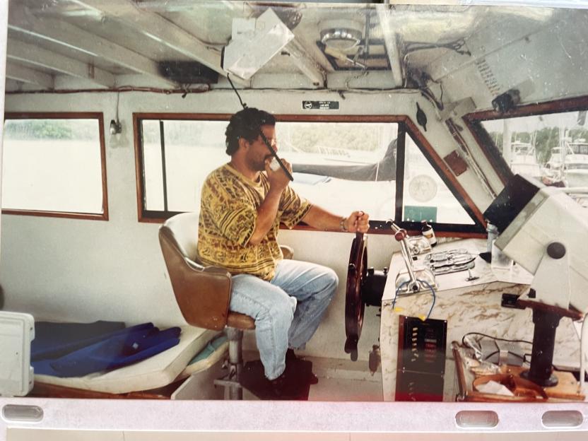 Martin Suarez at the helm of a boat, speaking into a radio.