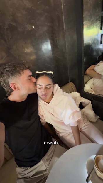 A man kissing a woman on the cheek; they are sitting together at a cafe table.
