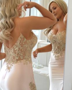 Woman admiring herself in a pink lace gown in a mirror.
