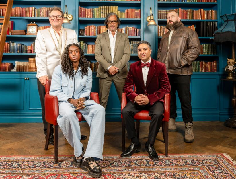 Five people in a library, two women are seated and three men are standing.