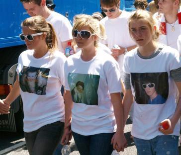 Three sisters holding hands at a protest against knife crime, wearing white t-shirts with photos of their murdered brother.