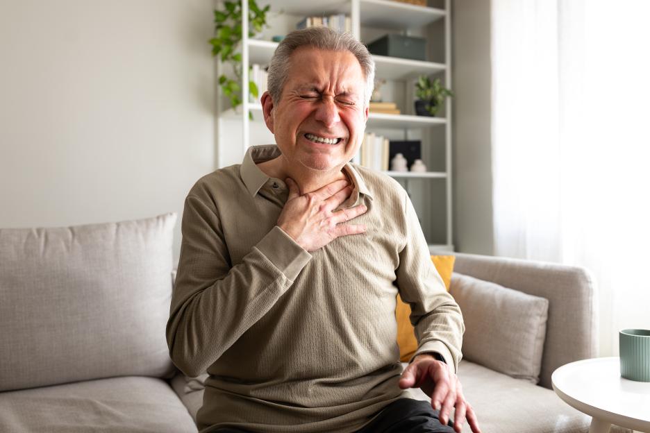 Senior man suffering chest pain or heart attack, sitting on a sofa.