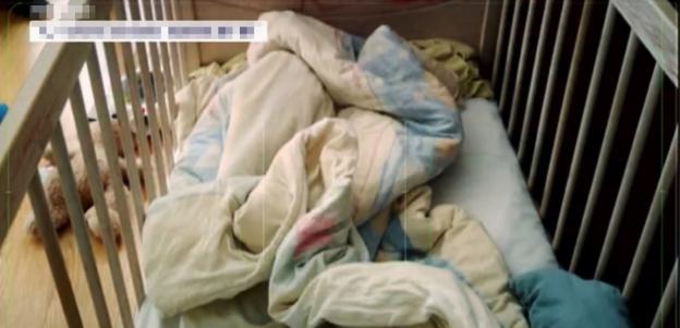Interior of a crib with bedding and a stuffed animal.