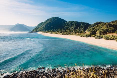 Tropical beach with turquoise water and green hills.