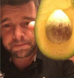 Man holding half an avocado in front of his face.