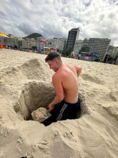 Man digging a hole in the sand on a beach.