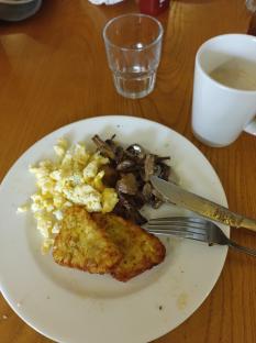 A plate of scrambled eggs, fried potatoes, and mushrooms.