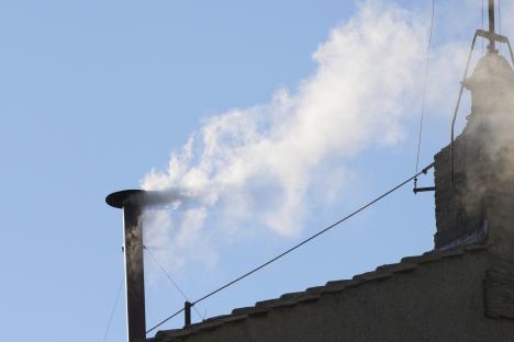 White smoke billowing from a chimney against a blue sky.