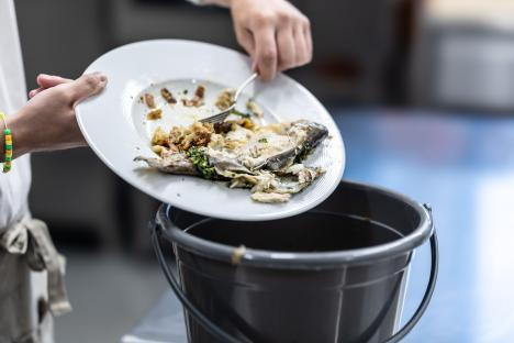 Person discarding leftover food into a trash can.