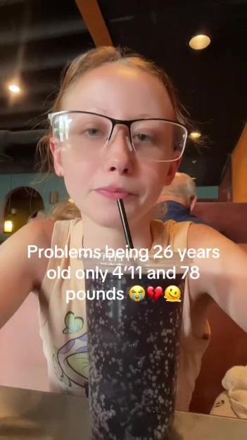 Young woman drinking from a large cup, expressing frustration about her height and weight.