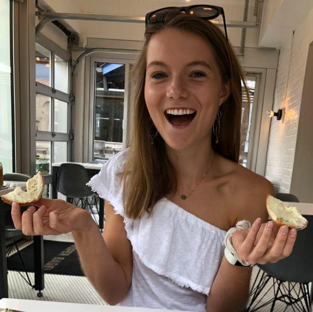 Woman happily holding two halves of a bagel with cream cheese.