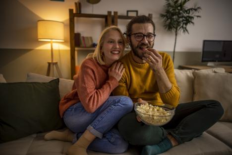 Couple watching TV and eating popcorn on a couch.