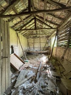 Interior of a dilapidated building with exposed wooden beams and brick walls.