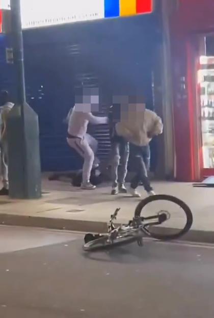 Four men in a street brawl, with a bicycle lying on its side in the foreground.
