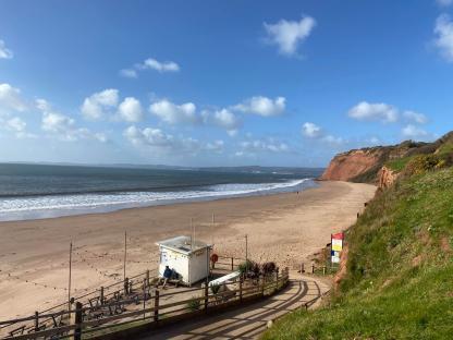 Sandy beach with a lifeguard hut and red cliffs under a blue sky.