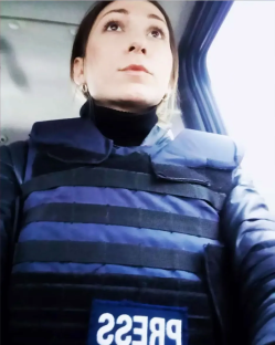 Woman in a press vest looking out a vehicle window.