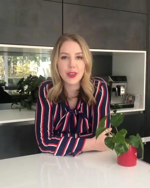 Katherine Ryan in a striped shirt sitting at a table with a plant.