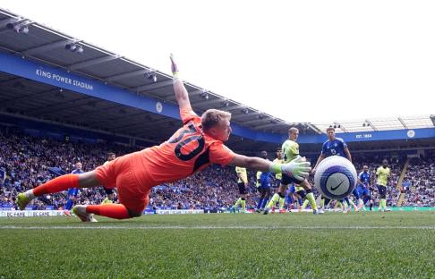 A soccer goalkeeper diving to stop a goal at the King Power Stadium.