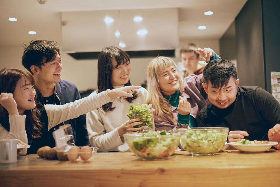 Roommates laughing together in a kitchen while preparing a meal.