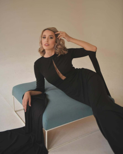 Woman in black dress posing on a teal ottoman.
