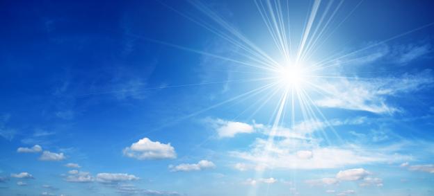 Bright sun shining in a blue sky with clouds.