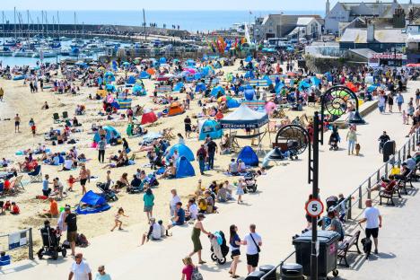 Crowded beach with people sunbathing, swimming, and relaxing.