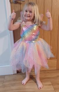 Girl in rainbow fairy costume giving thumbs up.